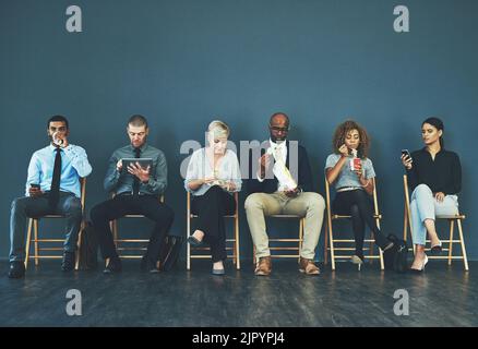 Nun, der Interviewer sagte, sich wohl zu fühlen... eine Gruppe gut gekleideter Geschäftsleute saß in der Schlange, während sie auf ein Interview warteten. Stockfoto