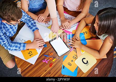 Einsatz von Technologie als zusätzliches Lehrmittel. High-Angle-Aufnahme einer Gruppe von nicht erkennbaren kleinen Kindern mit einem digitalen Tablet in der Schule. Stockfoto