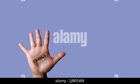 Wort zerbrechlich auf Hand isoliert auf blauem Hintergrund geschrieben Stockfoto