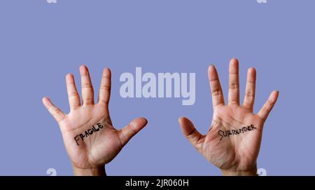 Wort zerbrechlich und Kapitulation auf Hand isoliert auf blauem Hintergrund geschrieben Stockfoto