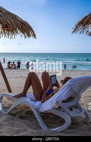 Eine Kubanerin im Urlaub am Strand von Varadero, Kuba; sie liest ein Buch auf ihrem Gerät von Kindesbeinen. Stockfoto