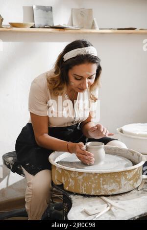 Potter Herstellung Schüssel auf dem Rad. Selbstständiger Töpferkünstler in kreativen Studio arbeiten mit rohem Ton Gestaltung handgemachte Tasse oder Glas. Fröhliche Keramikkunst Stockfoto