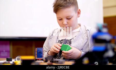 Der Junge von 11 Jahren spielt in dem Designer aus Würfeln, Platten, Schaltungen, Drähten. Ein kleiner Erfinder schafft Roboter, Maschinen aus verschiedenen Teilen des Designers. Hochwertige Fotos Stockfoto