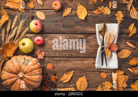 Herbsthintergrund mit Besteck, Kürbis, Äpfeln und Herbstlaub auf einem Holztisch. Stockfoto