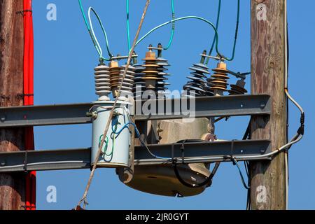 Ein großer, ölgefüllter Abschalttransformator, der an Hochspannungs-Oberleitungen angeschlossen ist, die 33.000 Volt tragen und auf etwa 440 Volt heruntersteigen. Stockfoto