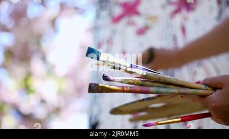 Nahaufnahme, weibliche Hände, Malerin, Künstlerin malt ein Bild von Blumen in blühenden Apfelplantagen, sie hält Palette mit Farben und Pinsel. Hochwertige Fotos Stockfoto