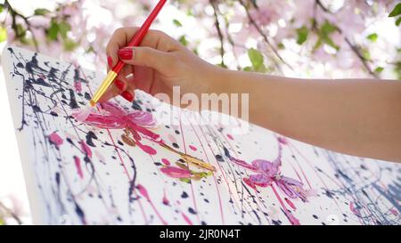 Nahaufnahme, weibliche Hand, Maler, Künstler malt ein Bild von Blumen in blühenden Frühling Apfelgarten, sie trägt Ölfarben auf Leinwand mit Pinsel, kreativen Prozess. Hochwertige Fotos Stockfoto