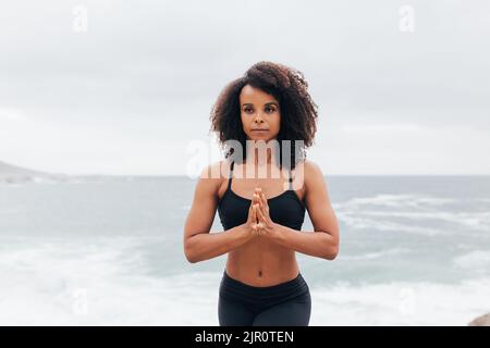 Junge Frau mit lockigen Haaren praktiziert Yoga-Meditation durch Ozean Stockfoto
