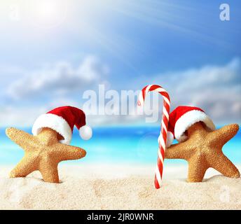 Seesterne im Weihnachtsmannhut und Süßigkeiten an einem Sommerstrand. Frohe Weihnachten. Stockfoto