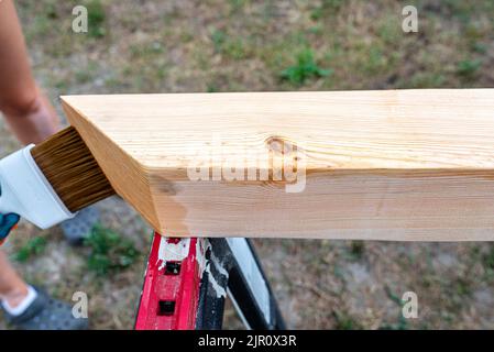 Die Frau imprägniert roh gehobelte Kiefernbalken mit Abmessungen von 100x100mm mit einer farblos imprägnierten. Stockfoto