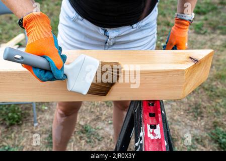 Die Frau imprägniert roh gehobelte Kiefernbalken mit Abmessungen von 100x100mm mit einer farblos imprägnierten. Stockfoto