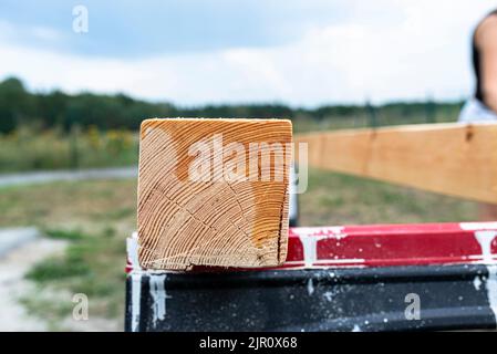 Die Frau imprägniert roh gehobelte Kiefernbalken mit Abmessungen von 100x100mm mit einer farblos imprägnierten. Stockfoto