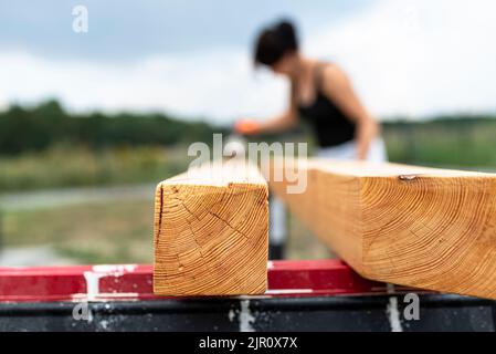 Die Frau imprägniert roh gehobelte Kiefernbalken mit Abmessungen von 100x100mm mit einer farblos imprägnierten. Stockfoto