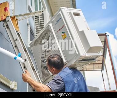 Ein Mann trägt einen schweren Klimaanlagenkompressor auf seiner Schulter, während er eine Leiter klettert. Stockfoto