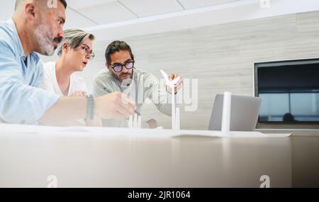 Team kreativer Designprofis, die mit 3D Windenergieanlagenmodellen in einem modernen Büro arbeiten. Eine Gruppe kreativer Geschäftsleute, die eine Diskussion führen Stockfoto