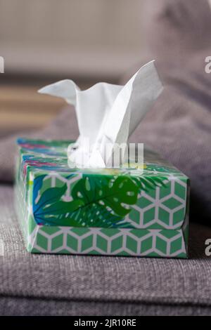 Ein Porträt einer bunten Schachtel Papiertaschentücher, die auf der Seite einer Couch in einem Wohnzimmer stehen, bereit, wenn Sie krank sind, eine Erkältung haben oder einfach nur Stockfoto