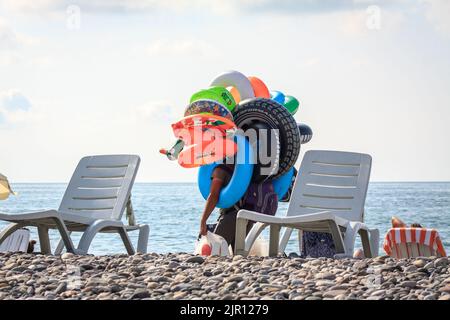 Ein Mann verkauft aufblasbares Spielzeug an einem Strand. Strandverkäufer. Batumi, Georgien - 2. Juli 2021 Stockfoto