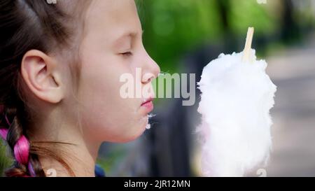 Portrait, hübsches Mädchen von acht Jahren, blond, mit Sommersprossen und bunten Zöpfen, isst süße weiße Baumwolle, Zuckerwatte, Kerzenfloss. Spaß haben, im Stadtpark, im Sommer. Hochwertige Fotos Stockfoto