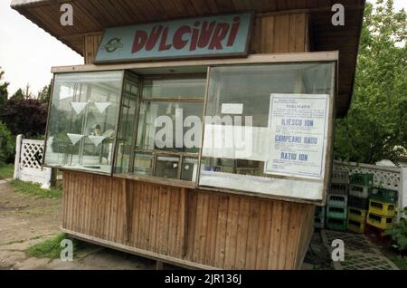 Mai 1990. Die ersten demokratischen Wahlen nach dem Fall des Kommunismus. Auf dem Vorderfenster eines Straßenladens zeigt ein Plakat den Namen der drei Konkurrenten: Ion Iliescu, Radu Campeanu & Ion Ratiu. Stockfoto