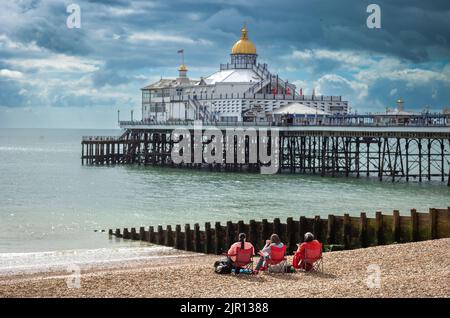 Drei Frauen sitzen auf Klappstühlen am Strand neben dem Eastbourne Pier in East Sussex, Großbritannien. Stockfoto