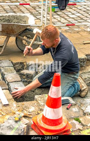 Dinan, Frankreich – 12. April 2022: Cobblestone Street. Ein Arbeiter pflasterte aus bemundeten Steinen auf der Auffahrt. Stockfoto