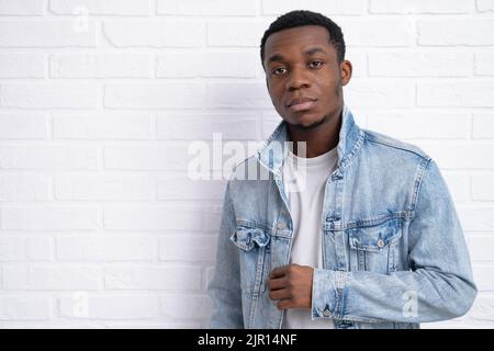 Portrait junger hübscher afrikanischer schwarzer Mann, der Jeansjacke an Backstein trägt und im Freien eine Wand mit Copyspace hat. Stockfoto