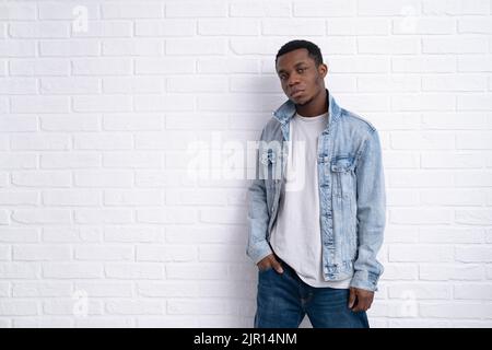 Portrait junger hübscher afrikanischer schwarzer Mann, der Jeansjacke an Backstein trägt und im Freien eine Wand mit Copyspace hat. Stockfoto