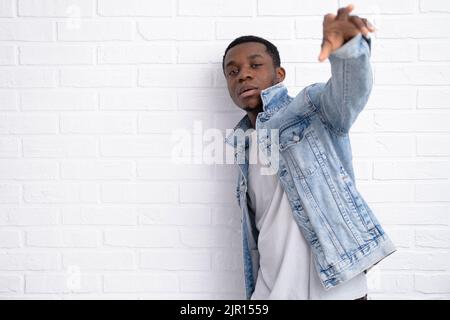 Portrait junger hübscher afrikanischer schwarzer Mann, der Jeansjacke an Backstein trägt und im Freien eine Wand mit Copyspace hat. Stockfoto