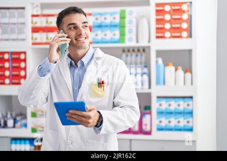 Junger hispanischer Apotheker, der mit dem Touchpad in der Apotheke auf dem Smartphone spricht Stockfoto