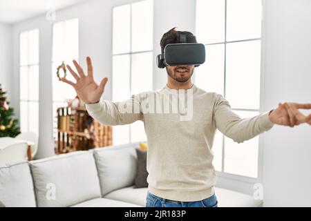 Junger hispanischer Mann lächelt glücklich mit 3d-VR-Brille zu Hause. Stockfoto