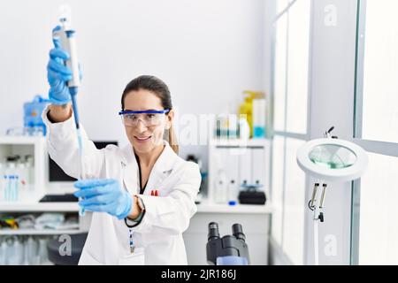 Junge hispanische Frau trägt Wissenschaftlerin Uniform mit Pipette im Labor Stockfoto