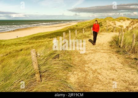 Eine Frau, die auf einem schönen sandigen Weg entlang des Meeres geht. Nordholland Dünenreservat, Egmond aan Zee, Niederlande. Stockfoto