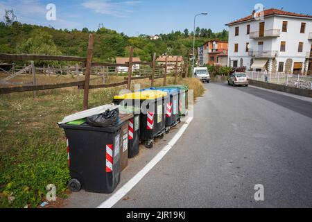 Eine Reihe verschiedenfarbiger Haushaltsabfallbehälter warten auf die Abholung am Straßenrand in der Nähe von Millesimo, Italien Stockfoto