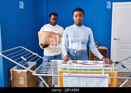 Junge afroamerikanische Paar hängende Kleidung an Wäscheleine Denken Haltung und nüchternen Ausdruck selbstbewusst aussehen Stockfoto