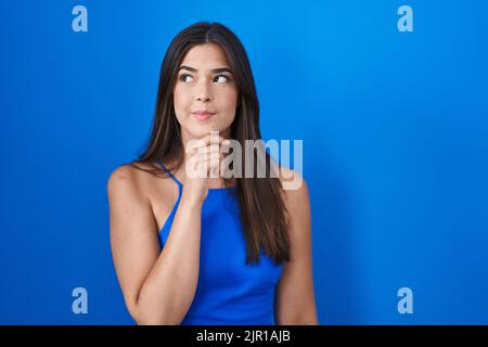 Hispanische Frau, die über blauem Hintergrund steht, denkt besorgt über eine Frage, besorgt und nervös mit der Hand am Kinn Stockfoto