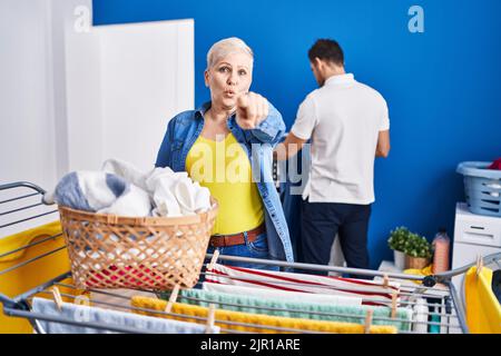 Hispanische Mutter und Sohn hängen Kleidung an der Wäscheleine, zeigen mit dem Finger auf die Kamera und auf Sie, selbstbewusste Geste, die ernst aussieht Stockfoto