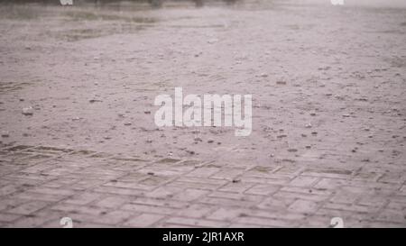 Nahaufnahme, es gibt starken Regen, eine Dusche, große schwere Tropfen Tropfen Tropfen Tropfen auf die Straßenfliesen. Regentropfen auf nasser Bodenstruktur, starke Regentropfen auf Asphalt. Wasserpfützen bei starkem Regen. Hochwertige Fotos Stockfoto