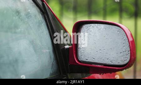 Nahaufnahme, auf den Autoglasscheiben Tropfen Tropfen Tropfen Tropfen Tropfen Tropfen Tropfen Tropfen Tropfen auf eine Vielzahl von Bächen. Tropfen Regen auf den Spiegel der Seitenansicht. Es gibt starken Regen, eine Dusche. Regentropfen auf dem Autoglas. Hochwertige Fotos Stockfoto