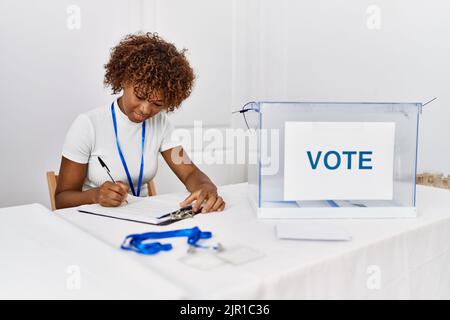 Junge afroamerikanische Frau, die am Wahlkollegium lächelnd selbstbewusst auf die Checkliste schreibt Stockfoto
