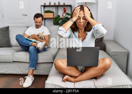 Hispanische Paar im mittleren Alter zu Hause, Frau mit Laptop leiden unter Kopfschmerzen verzweifelt und gestresst, weil Schmerzen und Migräne. Hände auf dem Kopf. Stockfoto