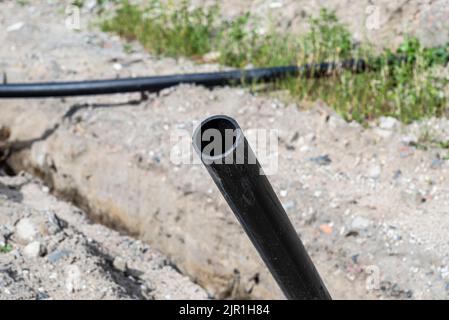 Offener Anfang der Kunststoff-Wasserleitung entlang des Grabens mit hohem Grundwasser, Wasseranschluss in der Siedlung. Stockfoto