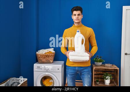 Junger hispanischer Mann hält saubere Handtücher entspannt mit ernstem Gesichtsausdruck. Einfach und natürlich auf die Kamera schauen. Stockfoto