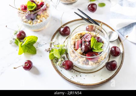 Gesundes Menükonzept. Hausgemachtes Müsli-Frühstück. Glas Parfait aus Müsli, Beerenkirsche, Joghurt mit Chiasamen auf rustikalem Tisch. Stockfoto