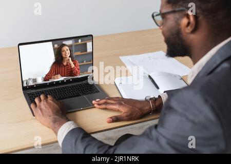 Online-Meeting. Schwarzer männlicher Unternehmer mit Videoanruf mit weiblicher Geschäftspartnerin Stockfoto