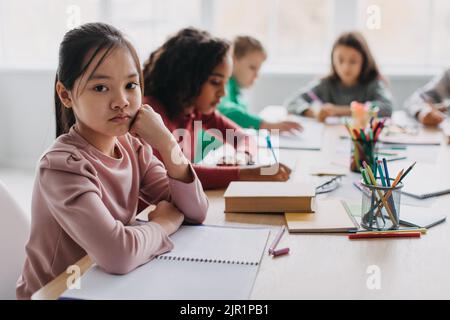 Traurig Asiatisch Schulmädchen Blick Auf Kamera Sitzen Im Modernen Klassenzimmer Stockfoto