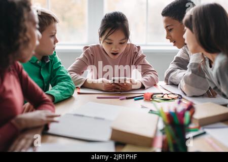 Klassenkameraden, Die Während Der Pause Im Klassenzimmer Smartphone Am Schreibtisch Sitzen Stockfoto