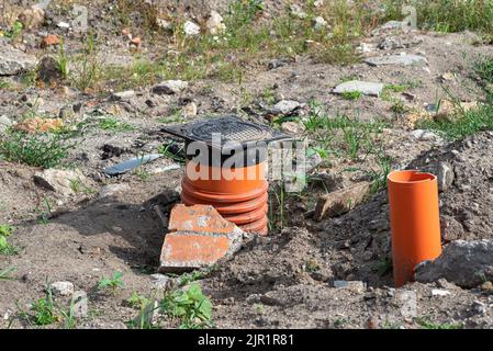 Inspektion der Abwasseranlage mit einem geschlossenen gusseisernen Schachtloch, sichtbaren Kunststoffrohren. Stockfoto