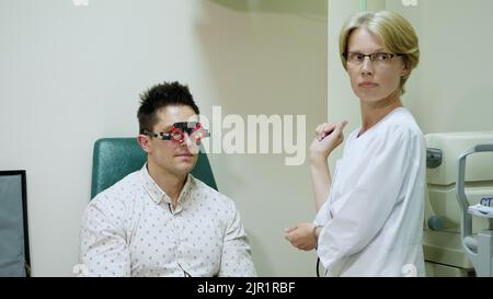 Die Ärztin der Augenheilkunde überprüft in einer modernen Klinik die Sehkraft eines gutaussehenden jungen Mannes. Arzt und Patient in der Augenklinik. Der Arzt gibt Ratschläge. Hochwertige Fotos Stockfoto