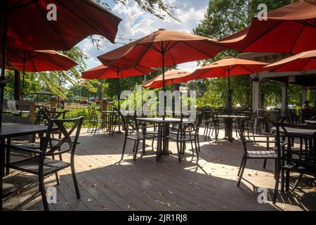 Athens, NY - USA - 4. Aug 2022 Landschaftsansicht der mit rotem Regenschirm bedeckten Cafétische im Essbereich im Freien des River Grill, einem Café am Wasser Stockfoto