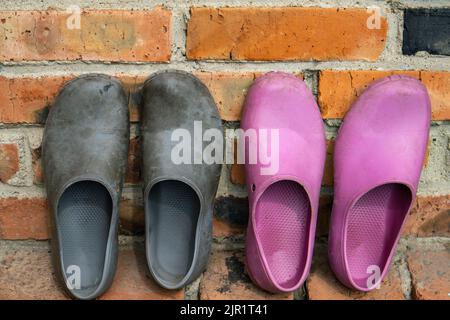 Zwei Paar Gummi-Galoschen in Schwarz und Pink auf dem Hintergrund einer alten Ziegelwand Stockfoto